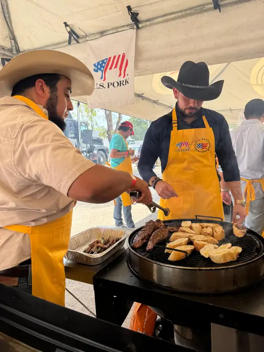 Dos parrilleros con mandil amarillo asando carne y pan en la plancha
